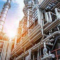 Industrial factory with heavy piping and security fencing.